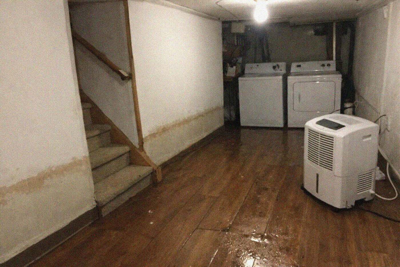 The flooded basement of a Brooklyn row house with water across the floor and a washer and dryer standing in it