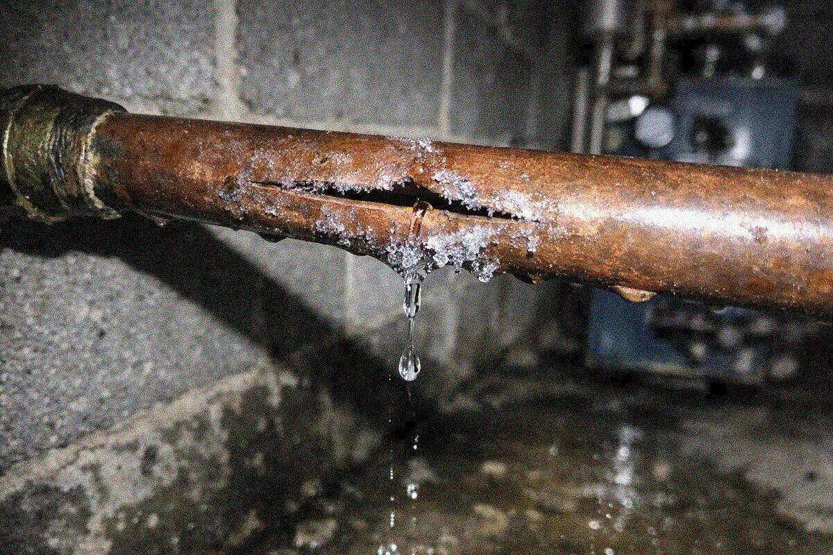 A split copper supply pipe in an unfinished basement ceiling with water running down the foundation wall below it