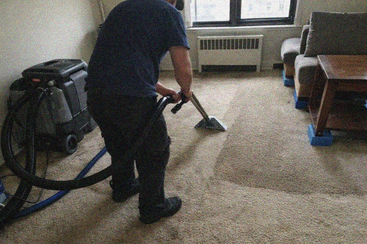 A portable extractor with a wand being drawn across the wet floor of a Manhattan apartment living room