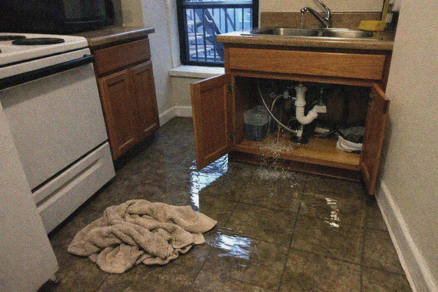 A New York apartment kitchen with standing water across the tile floor and the base of the cabinets sitting in it