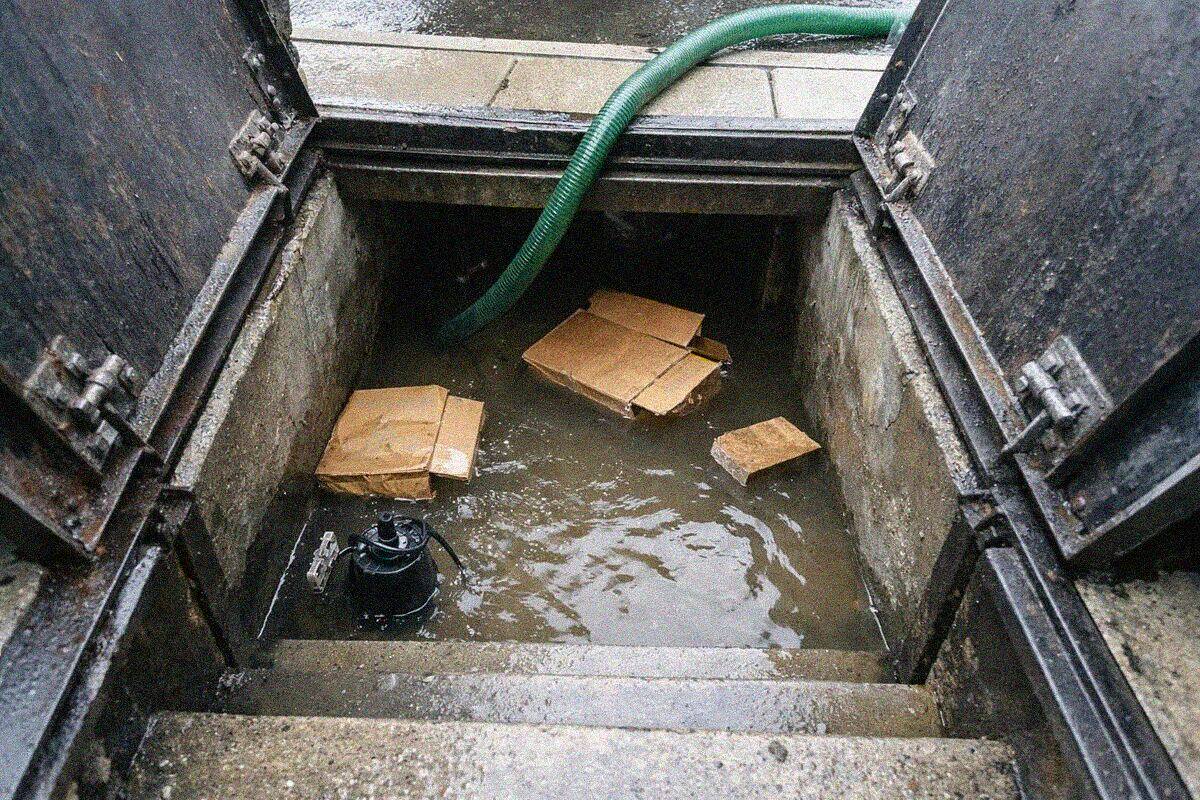 A steel sidewalk hatch open onto the steps of a flooded Brooklyn cellar with water on the bottom treads