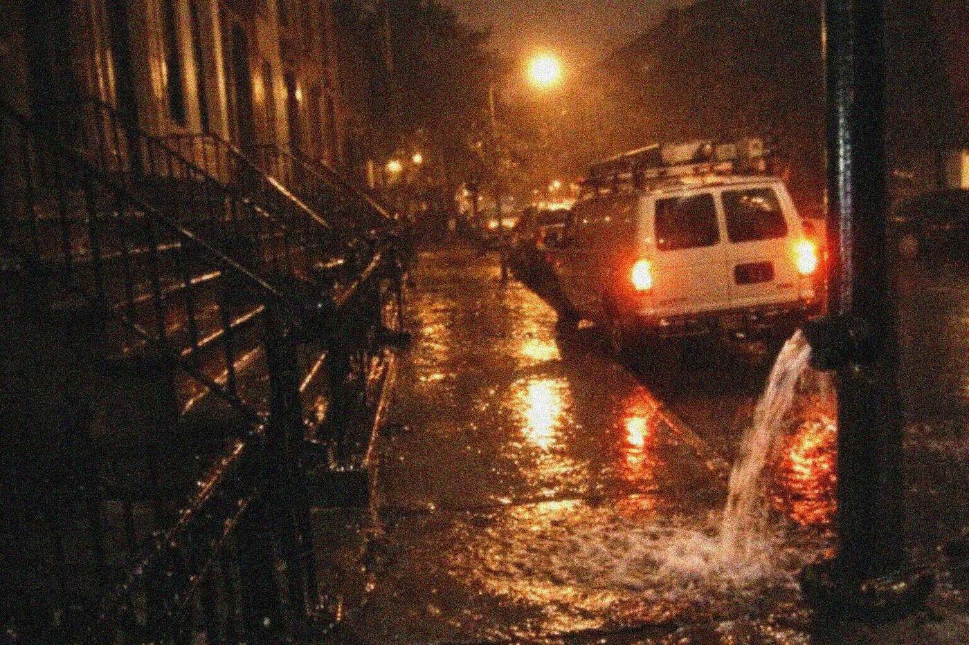 Brownstone block in New York at night with heavy rain running down the stoops and along the gutter
