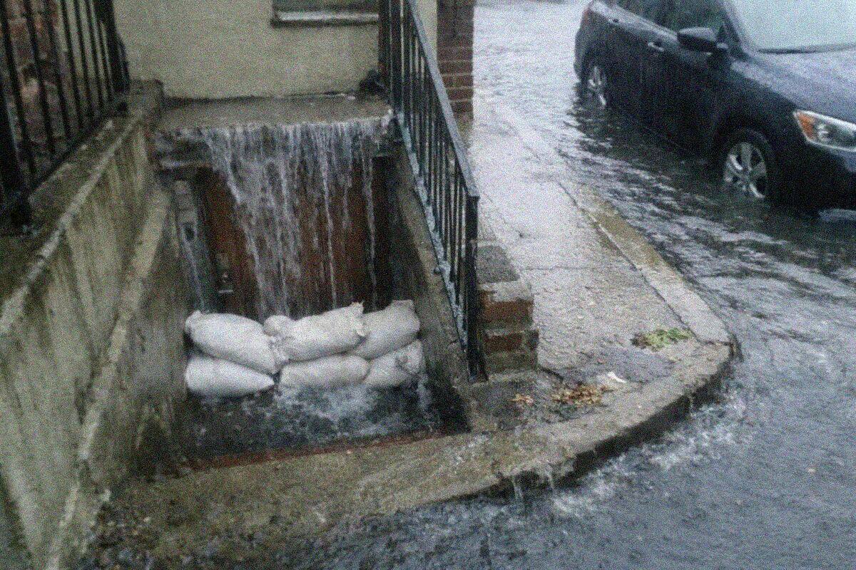 Storm water pouring down the exterior steps into a basement apartment doorway in Queens